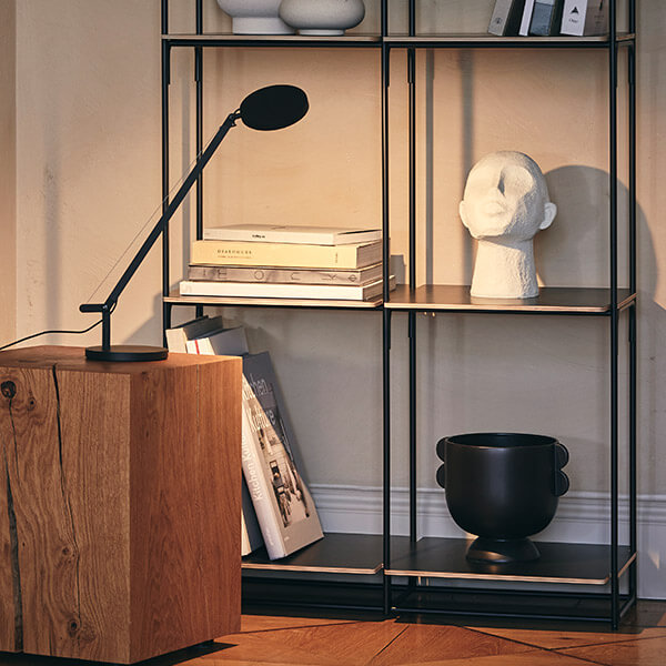 Artemide Demetra Micro LED table lamp on a side table with bookshelf in the background